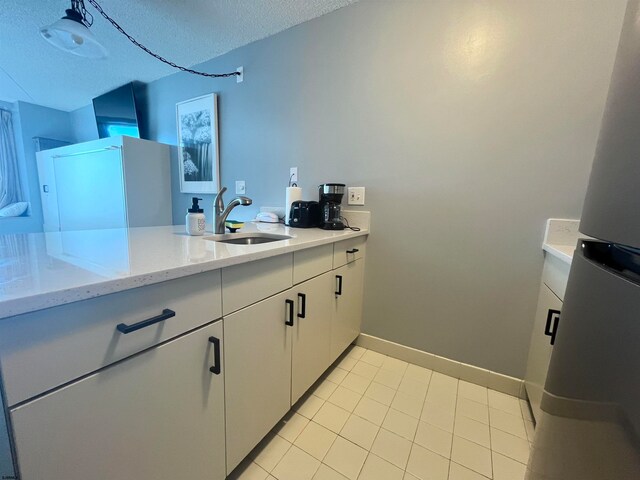 kitchen featuring light stone counters, a textured ceiling, sink, white cabinets, and stainless steel fridge