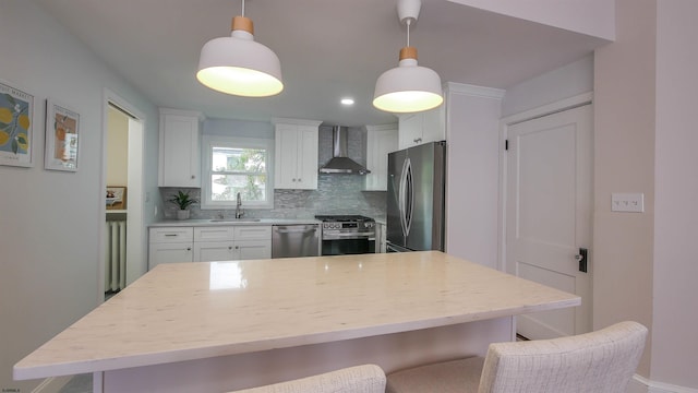 kitchen featuring wall chimney range hood, pendant lighting, decorative backsplash, appliances with stainless steel finishes, and white cabinetry