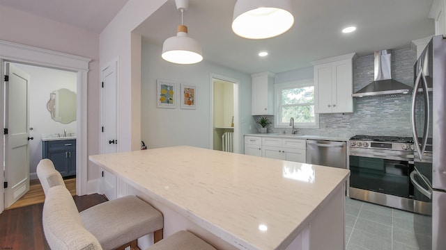 kitchen featuring white cabinets, sink, wall chimney exhaust hood, decorative light fixtures, and appliances with stainless steel finishes