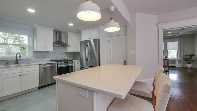 kitchen featuring stainless steel appliances, sink, wall chimney range hood, light hardwood / wood-style flooring, and decorative light fixtures