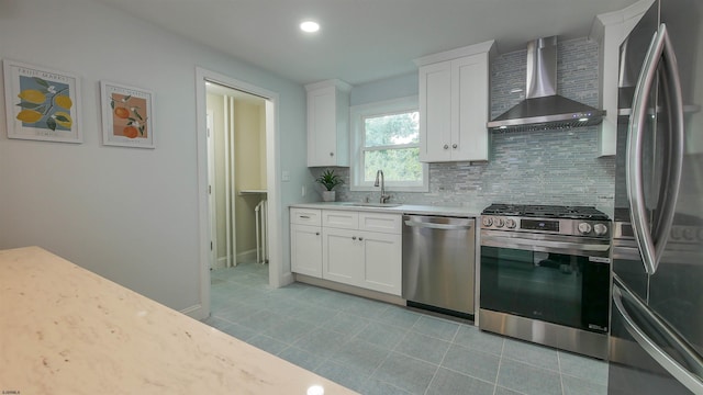 kitchen featuring wall chimney range hood, white cabinetry, sink, and stainless steel appliances