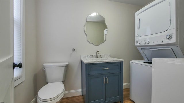 bathroom featuring stacked washer and dryer, hardwood / wood-style flooring, vanity, and toilet