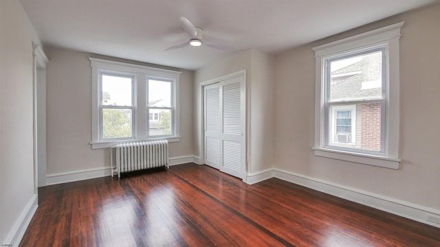 unfurnished bedroom with multiple windows, ceiling fan, radiator, and dark hardwood / wood-style flooring