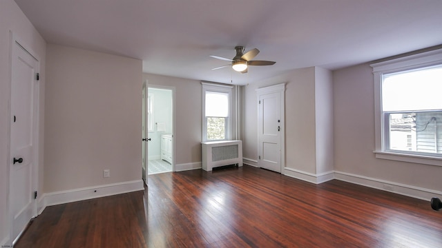 unfurnished bedroom featuring ceiling fan, ensuite bathroom, dark wood-type flooring, and radiator heating unit