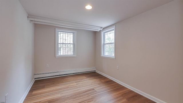 unfurnished room featuring baseboard heating, light wood-type flooring, and a wealth of natural light