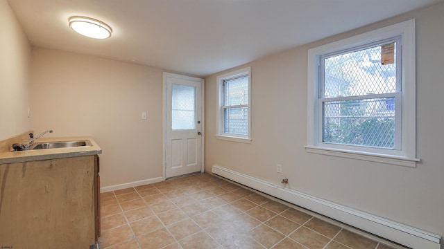 laundry area with baseboard heating, sink, light tile patterned floors, and a healthy amount of sunlight