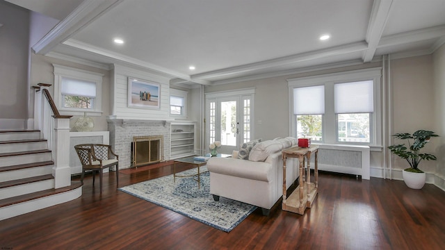 living room with radiator, beamed ceiling, a stone fireplace, dark wood-type flooring, and crown molding