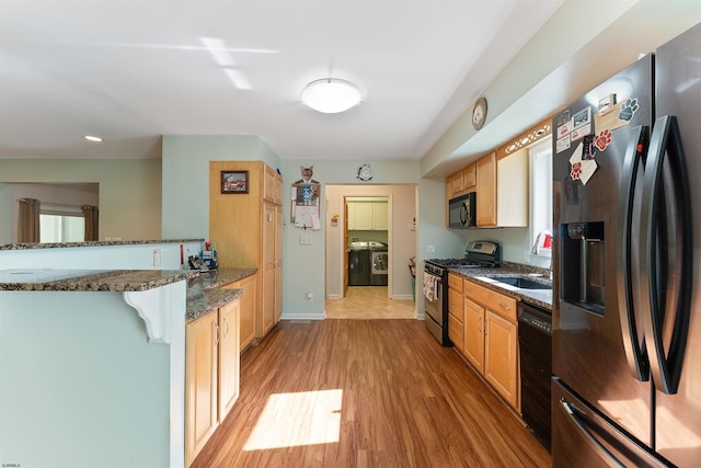 kitchen with sink, kitchen peninsula, black appliances, dark stone countertops, and light wood-type flooring