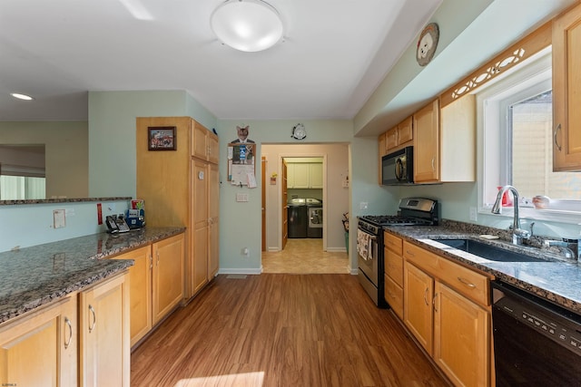 kitchen with wood-type flooring, dark stone counters, sink, washer / clothes dryer, and black appliances