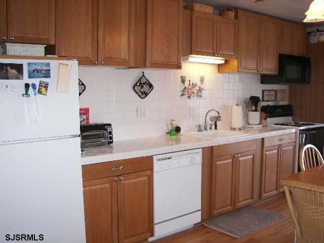 kitchen with tasteful backsplash, white appliances, sink, and light wood-type flooring