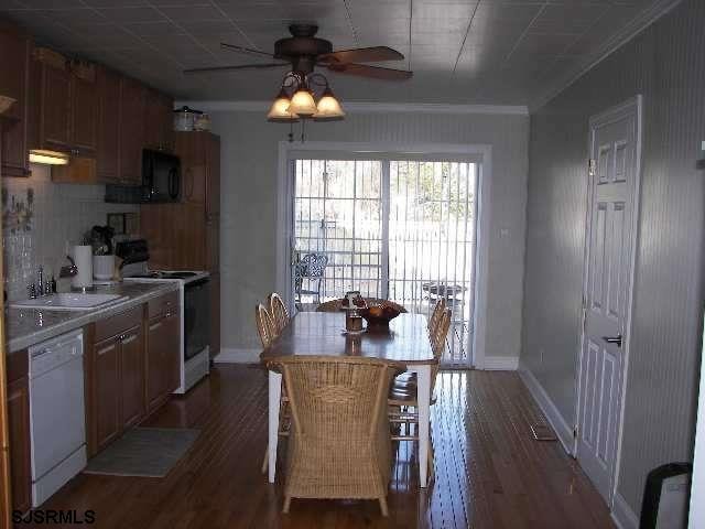 kitchen featuring ceiling fan, white appliances, dark wood-type flooring, ornamental molding, and a kitchen bar