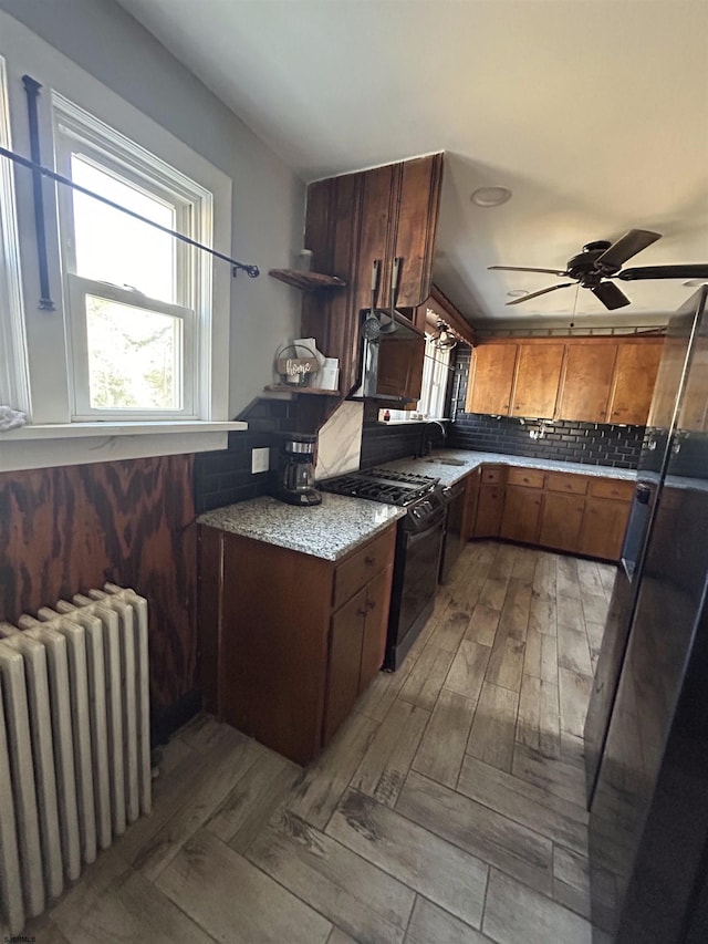 kitchen featuring ceiling fan, backsplash, radiator heating unit, and black gas range oven