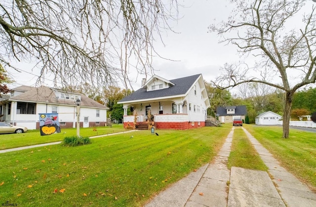 view of front of house with a porch, a front yard, and an outbuilding