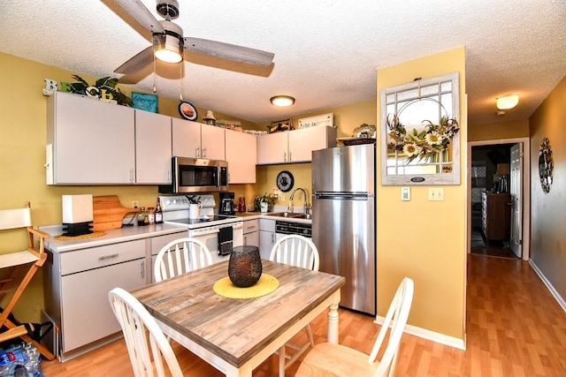 kitchen with appliances with stainless steel finishes, a textured ceiling, sink, and light hardwood / wood-style flooring