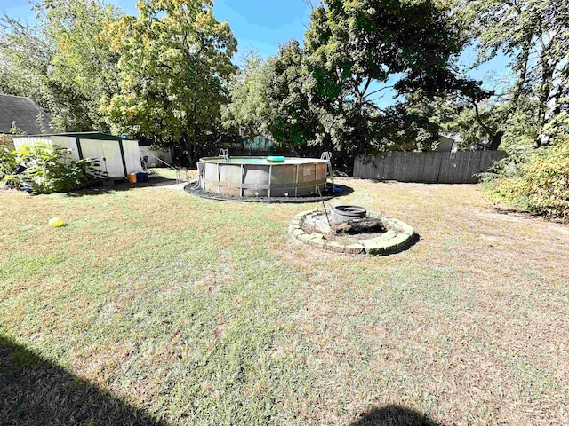 view of yard featuring a fenced in pool, a shed, and a fire pit