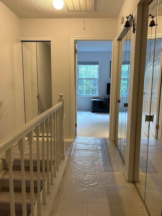 hallway with light carpet and a textured ceiling