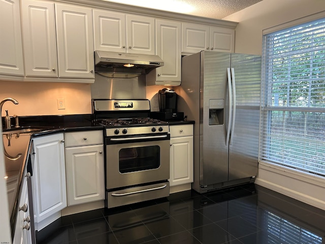 kitchen with a textured ceiling, dark tile patterned floors, stainless steel appliances, and white cabinets