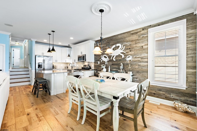 dining area featuring ornamental molding, a notable chandelier, wood walls, and light hardwood / wood-style floors