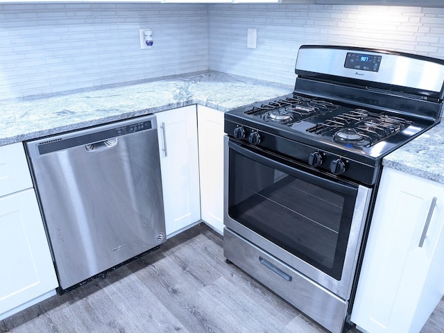 kitchen featuring wood-type flooring, white cabinets, appliances with stainless steel finishes, and light stone counters