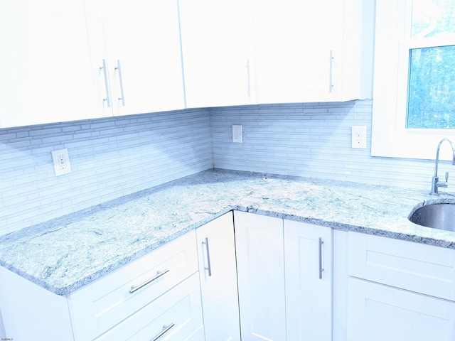 kitchen with light stone countertops, sink, decorative backsplash, and white cabinetry