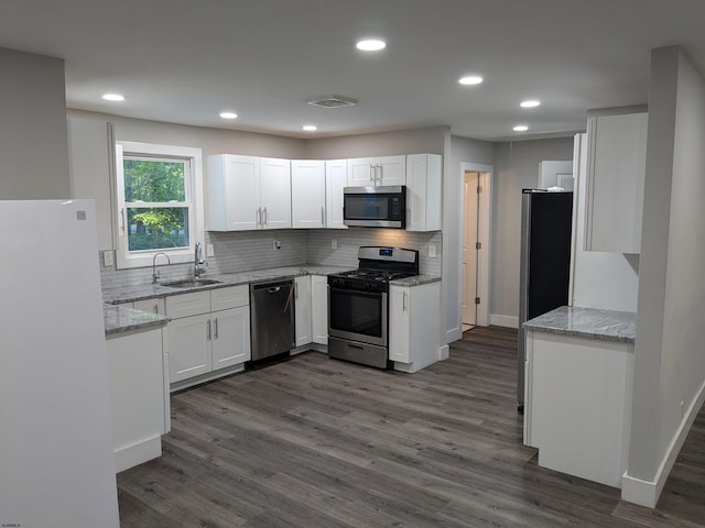 kitchen with white cabinets, appliances with stainless steel finishes, dark hardwood / wood-style flooring, and light stone countertops