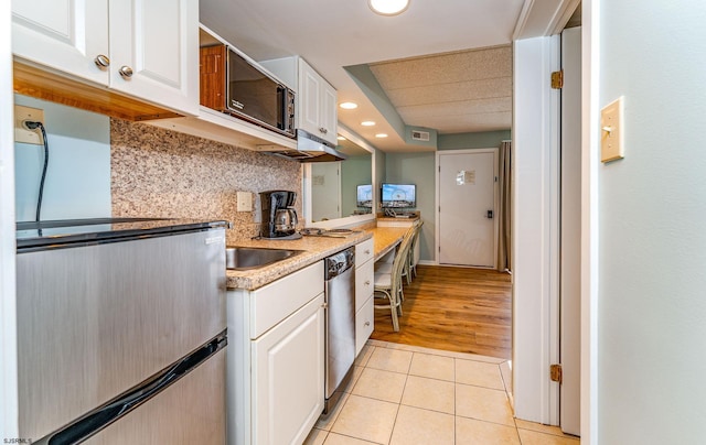 kitchen featuring tasteful backsplash, sink, dishwasher, light tile patterned floors, and white cabinetry