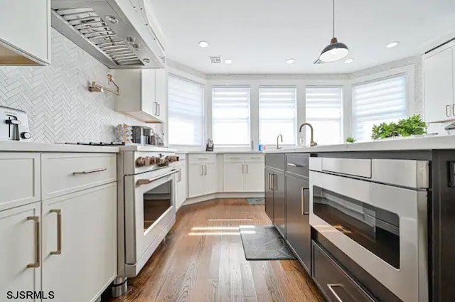 kitchen with hanging light fixtures, dark wood-type flooring, white cabinetry, high end stove, and range hood