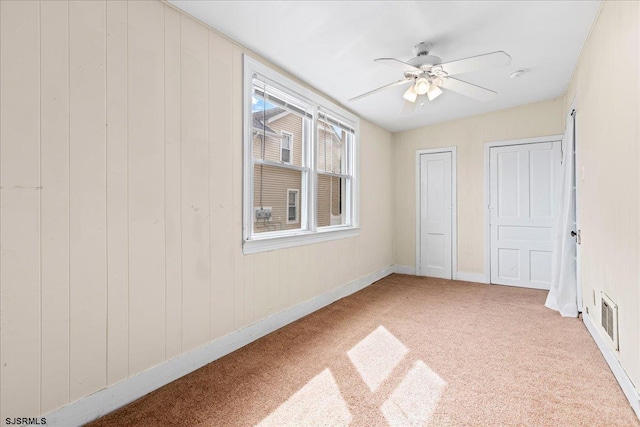 unfurnished bedroom featuring ceiling fan, wood walls, two closets, and carpet flooring