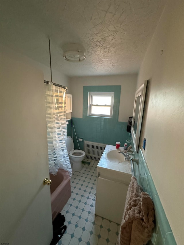 bathroom with a tub to relax in, radiator heating unit, vanity, toilet, and a textured ceiling