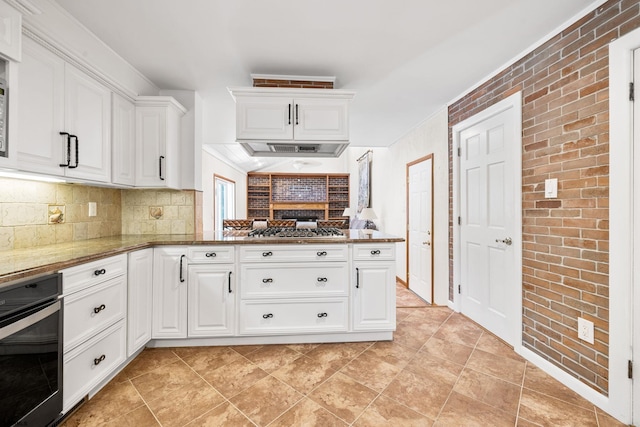 kitchen featuring stone counters, appliances with stainless steel finishes, kitchen peninsula, white cabinets, and brick wall