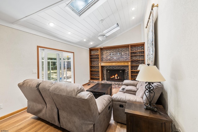 living room featuring light wood-type flooring, a fireplace, wooden ceiling, vaulted ceiling with skylight, and crown molding