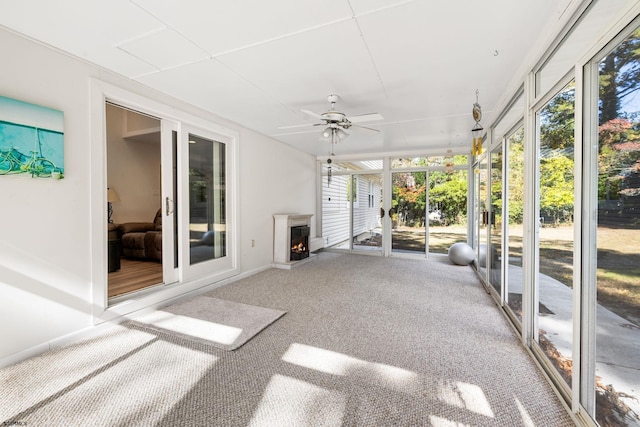 unfurnished sunroom with ceiling fan and a wood stove