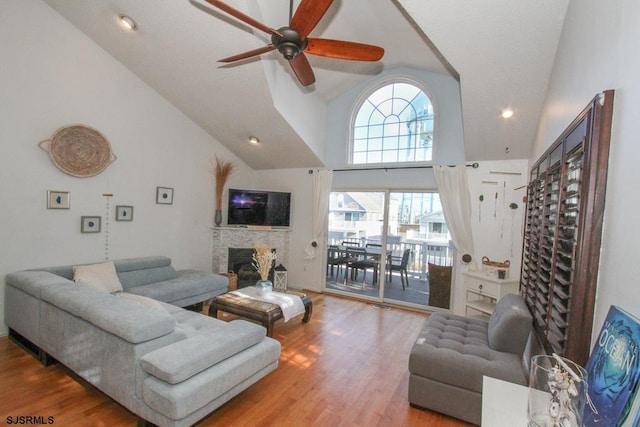 living room with a stone fireplace, hardwood / wood-style flooring, high vaulted ceiling, and ceiling fan