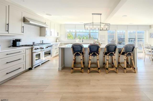 kitchen with a center island, double oven range, light wood-type flooring, white cabinetry, and extractor fan