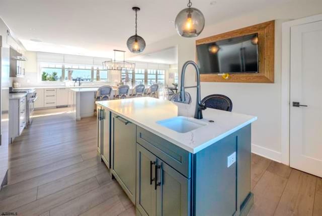 kitchen with stainless steel range, light wood-type flooring, decorative light fixtures, and a kitchen island with sink