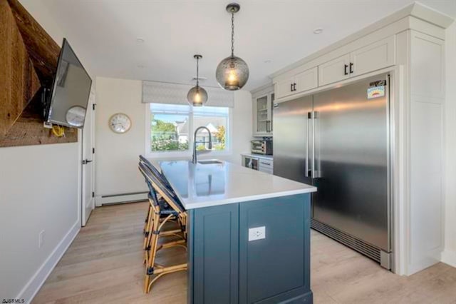 kitchen with pendant lighting, white cabinetry, stainless steel built in fridge, and a center island with sink