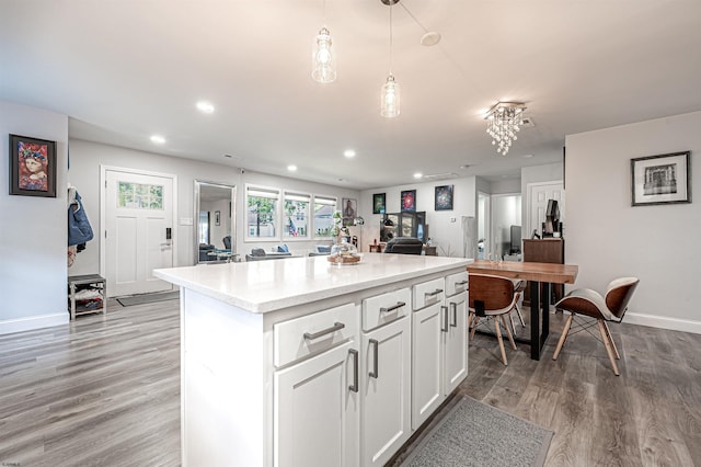 kitchen with light stone countertops, light wood-type flooring, a kitchen island, white cabinetry, and decorative light fixtures