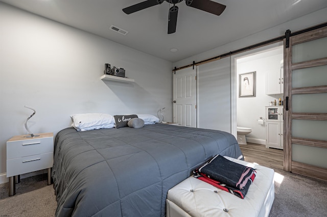 carpeted bedroom with ceiling fan, ensuite bathroom, and a barn door