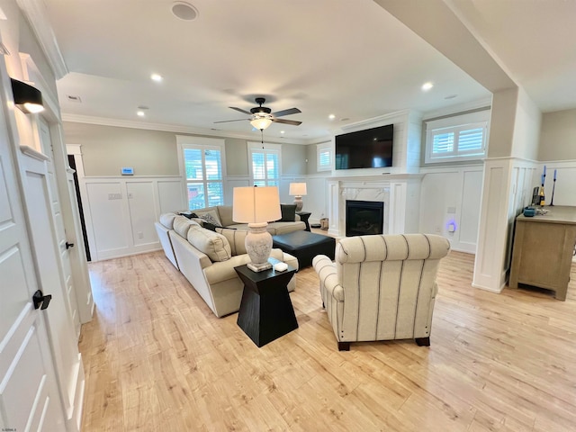 living room featuring light hardwood / wood-style flooring, ornamental molding, ceiling fan, and a high end fireplace