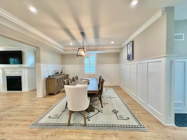 dining space with ornamental molding, light hardwood / wood-style flooring, and a premium fireplace