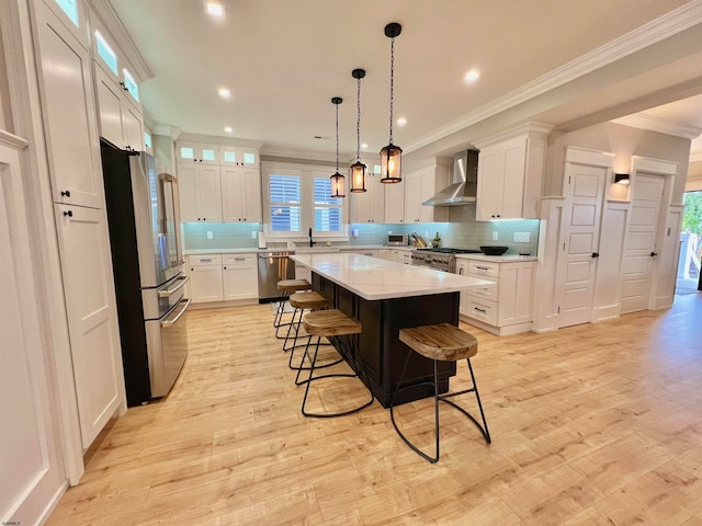 kitchen with wall chimney range hood, light wood-type flooring, a kitchen island, white cabinetry, and stainless steel appliances