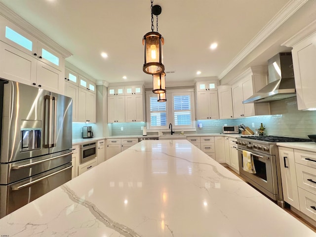 kitchen featuring wall chimney exhaust hood, stainless steel appliances, light stone countertops, pendant lighting, and white cabinetry