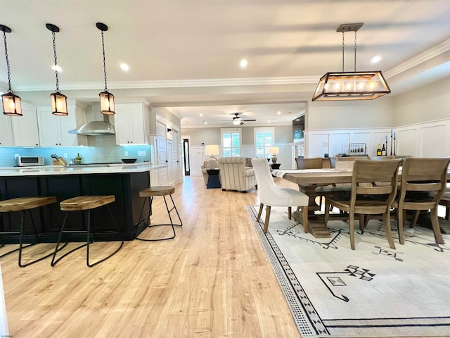 dining space featuring ornamental molding, light hardwood / wood-style flooring, and ceiling fan with notable chandelier