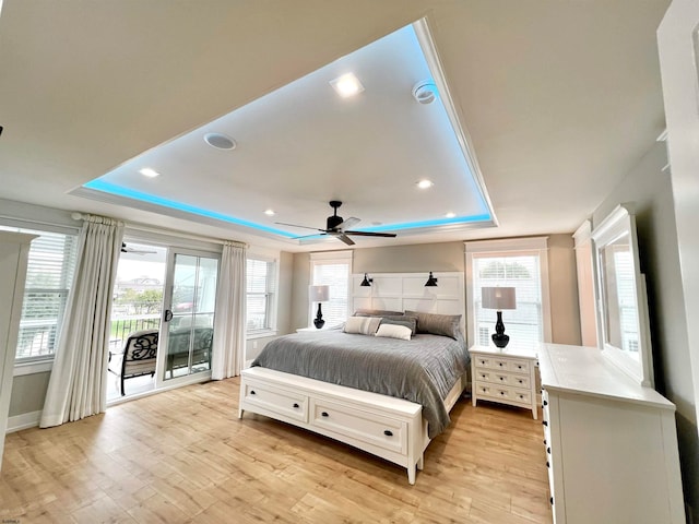 bedroom with light hardwood / wood-style flooring, a raised ceiling, multiple windows, and access to exterior