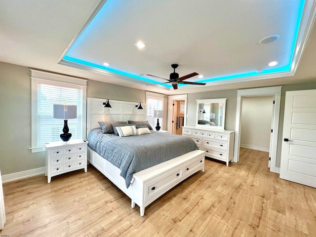 bedroom with ceiling fan, light wood-type flooring, and a raised ceiling