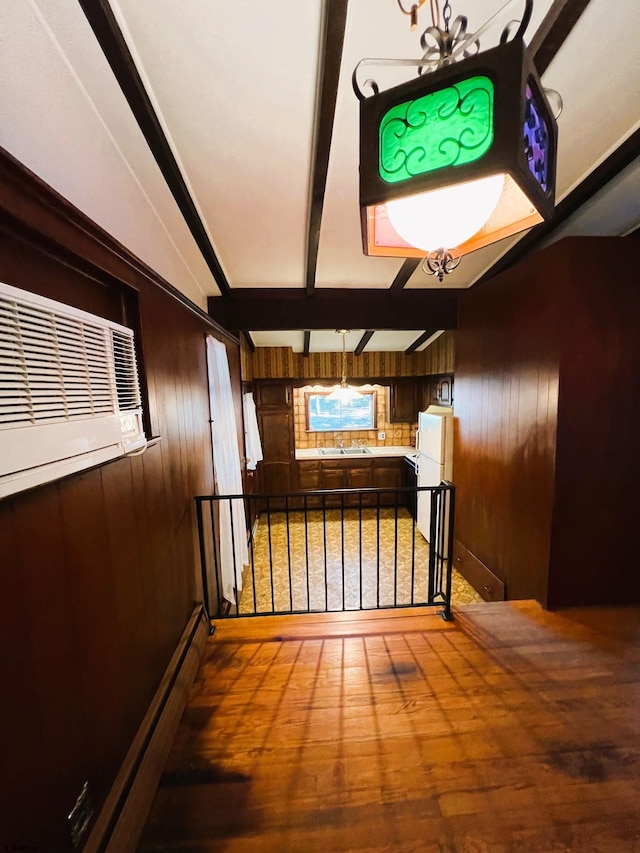 hallway with sink, beamed ceiling, wood-type flooring, and wooden walls