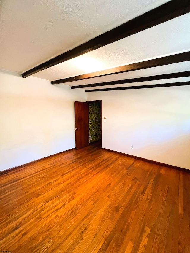 empty room featuring a textured ceiling, beamed ceiling, and wood-type flooring