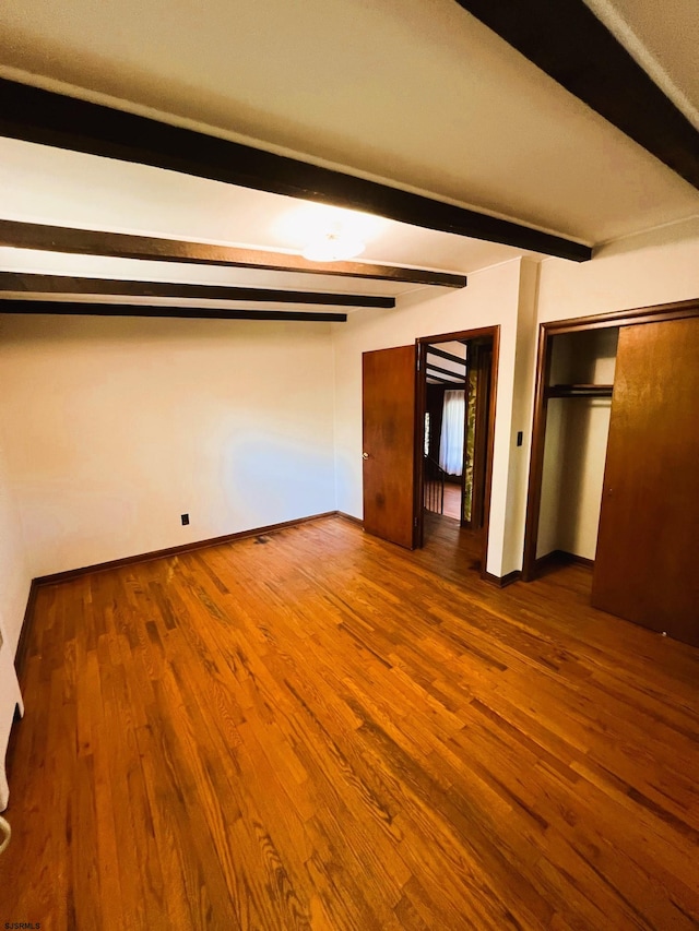 unfurnished bedroom featuring beam ceiling and hardwood / wood-style floors