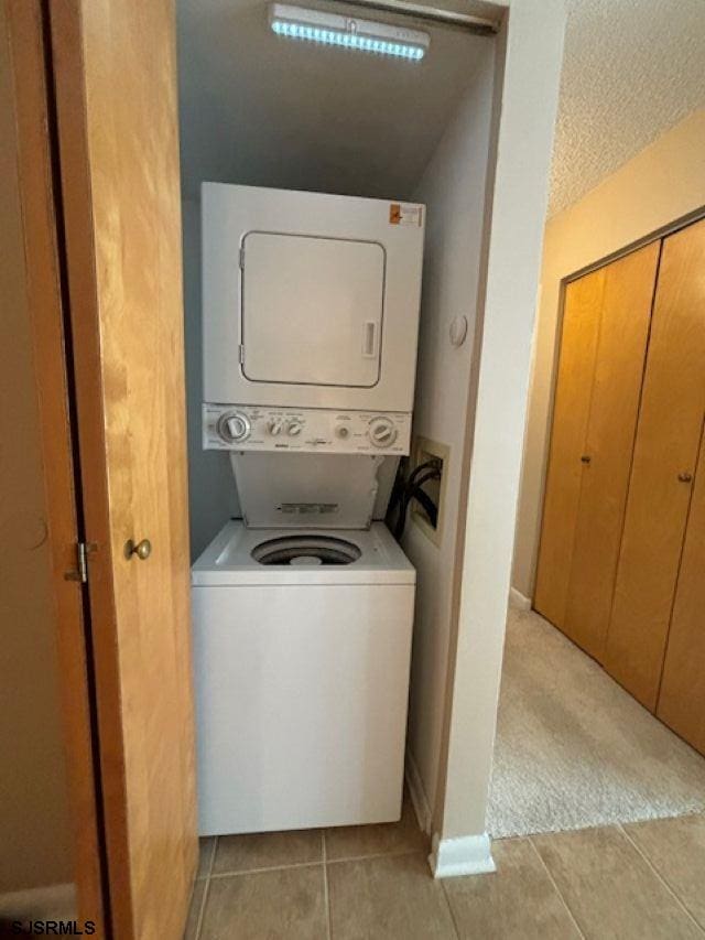 washroom with light carpet, laundry area, light tile patterned floors, stacked washer / dryer, and a textured ceiling