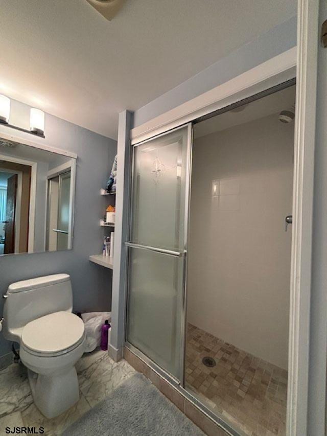 bathroom with marble finish floor, a shower stall, and toilet